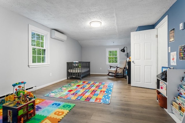 bedroom with wood finished floors, a textured ceiling, a wall mounted air conditioner, baseboard heating, and a nursery area