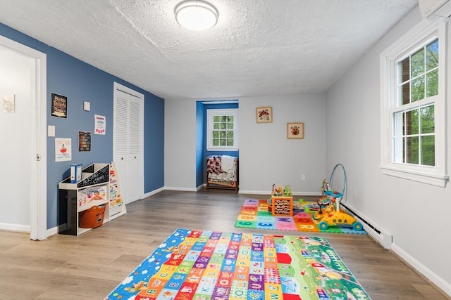 recreation room featuring baseboard heating, a textured ceiling, wood finished floors, and plenty of natural light