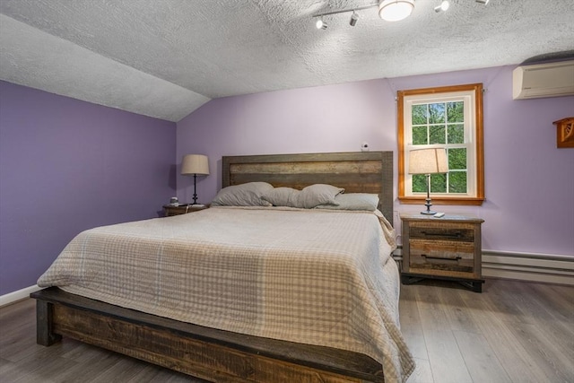 bedroom with a wall mounted AC, a baseboard heating unit, wood finished floors, a textured ceiling, and baseboards