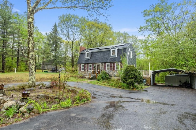 colonial inspired home with a gambrel roof, asphalt driveway, a carport, and a chimney