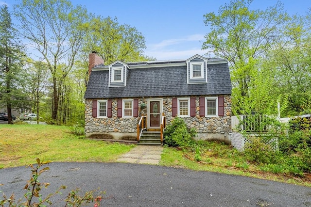 colonial inspired home with stone siding, a chimney, roof with shingles, and a front lawn