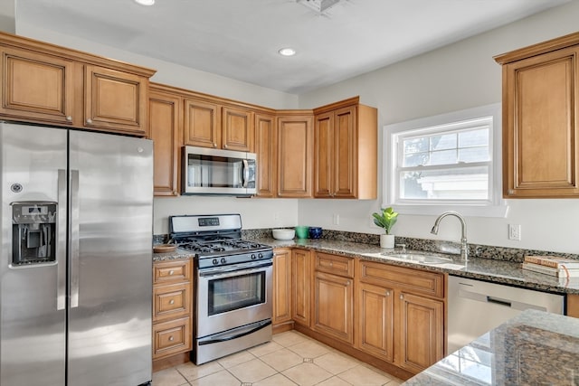 kitchen with dark stone countertops, light tile patterned flooring, stainless steel appliances, and sink