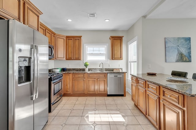 kitchen with dark stone countertops, sink, stainless steel appliances, and light tile patterned floors