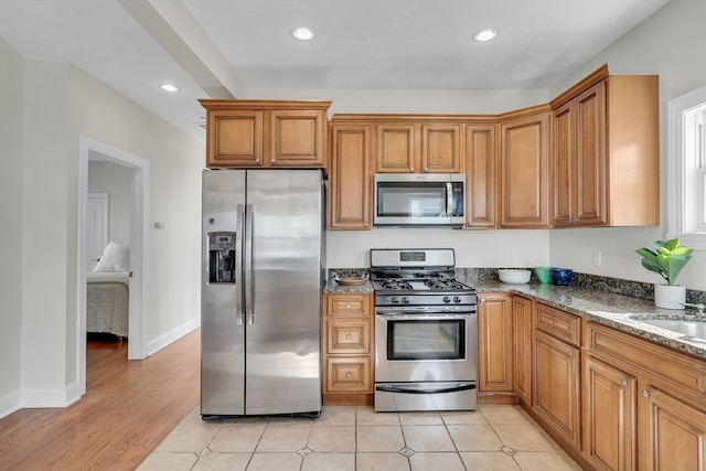 kitchen featuring dark stone countertops, sink, stainless steel appliances, and light hardwood / wood-style flooring