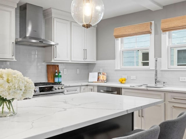 kitchen with sink, hanging light fixtures, appliances with stainless steel finishes, wall chimney range hood, and white cabinets