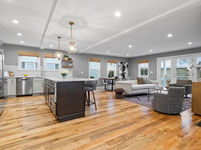 kitchen featuring wall oven, light hardwood / wood-style floors, a kitchen bar, decorative light fixtures, and stainless steel dishwasher