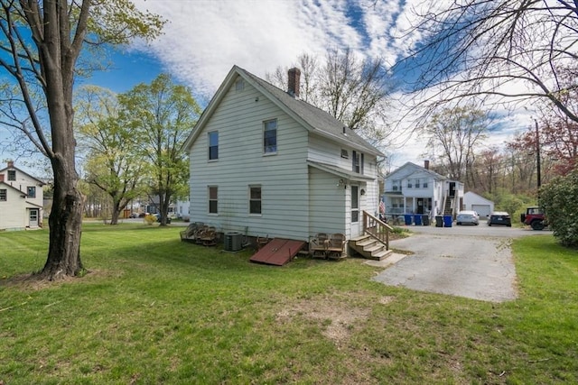 back of property with a chimney, cooling unit, and a lawn