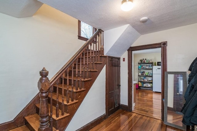 staircase featuring baseboards, hardwood / wood-style floors, and a textured ceiling