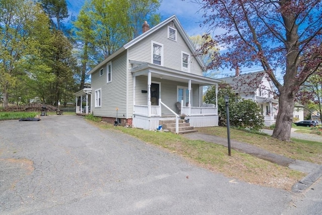 view of front of property with a chimney, aphalt driveway, and covered porch