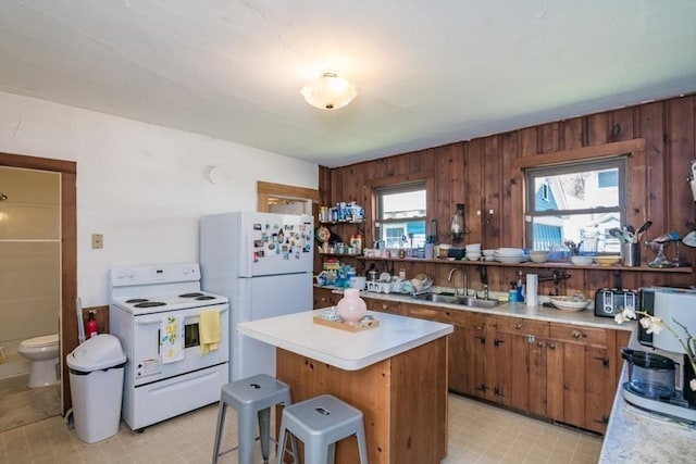 kitchen with a center island, brown cabinets, a sink, white appliances, and light countertops