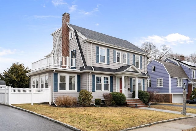 view of front of property featuring roof with shingles, a chimney, a gambrel roof, fence, and a balcony