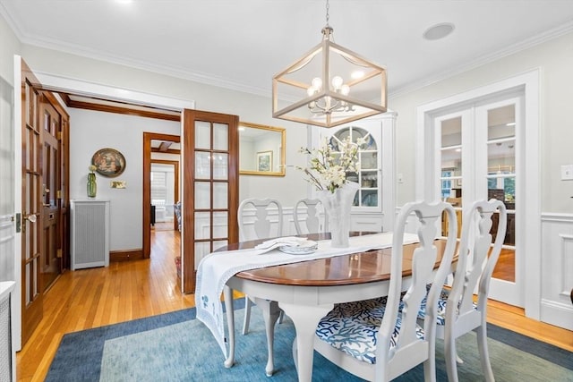 dining area with ornamental molding, french doors, an inviting chandelier, and light wood-style floors