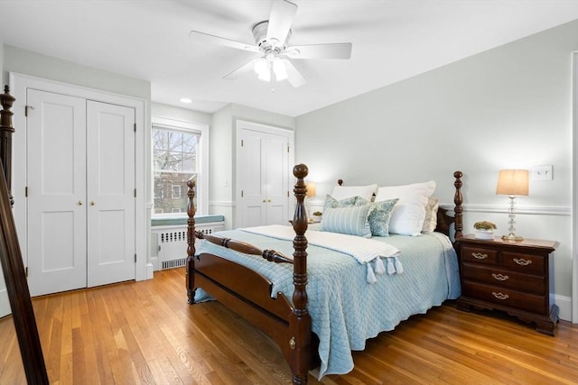 bedroom featuring radiator, light wood-style floors, a ceiling fan, and two closets