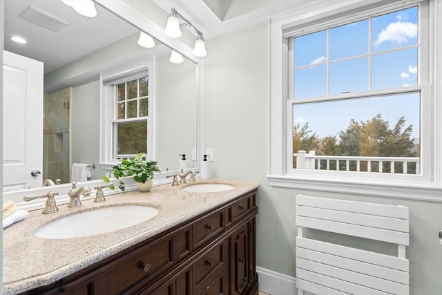 bathroom featuring double vanity, a shower with door, visible vents, and a sink