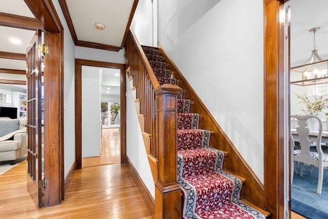 stairway featuring crown molding, baseboards, wood finished floors, and a notable chandelier