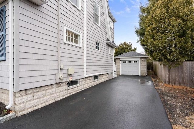 view of property exterior featuring aphalt driveway, an outbuilding, fence, and a garage