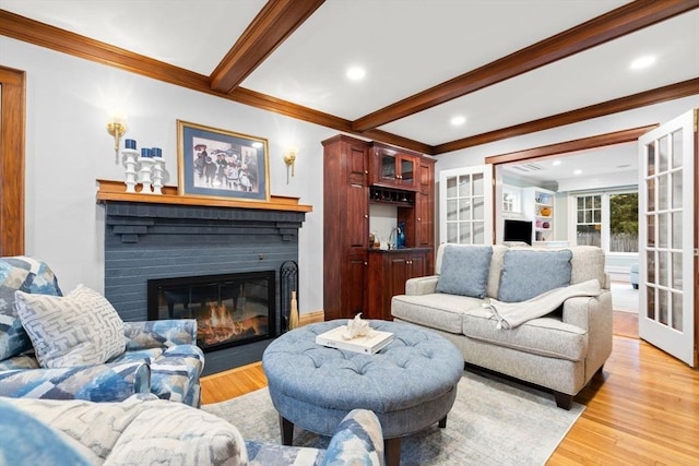 living area featuring light wood finished floors, a fireplace with flush hearth, ornamental molding, and beamed ceiling