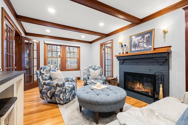 living area featuring light wood-type flooring, ornamental molding, a fireplace, and beam ceiling