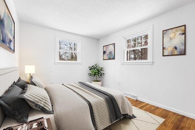 bedroom featuring wood-type flooring, multiple windows, visible vents, and baseboards