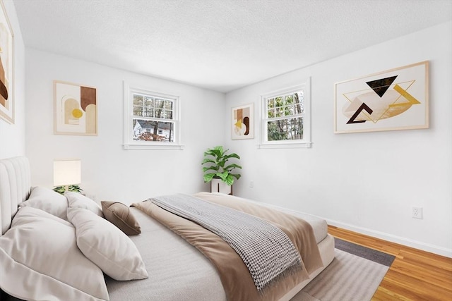 bedroom with a textured ceiling, wood finished floors, and baseboards