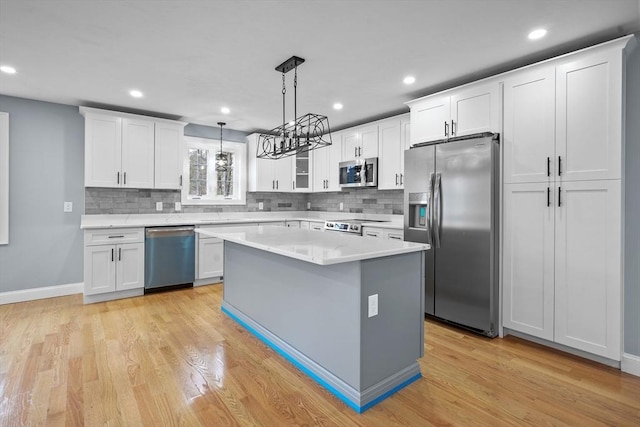 kitchen with decorative light fixtures, a center island, white cabinetry, light wood-type flooring, and stainless steel appliances