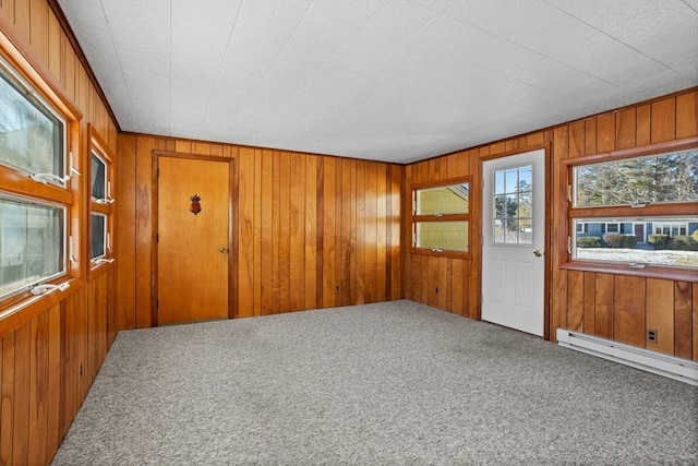 carpeted spare room with baseboard heating and wood walls