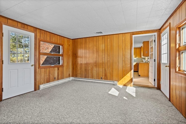 unfurnished room with a baseboard heating unit, light colored carpet, and wood walls