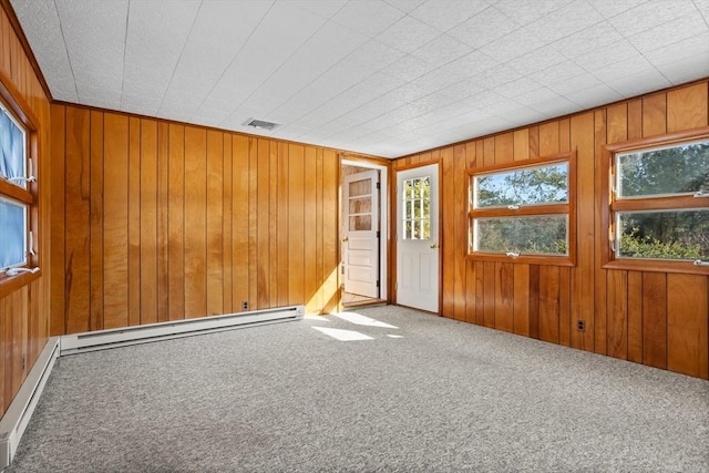 spare room with a baseboard radiator, carpet flooring, and wood walls