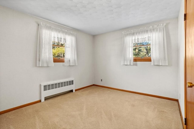 carpeted spare room featuring a wealth of natural light and radiator heating unit