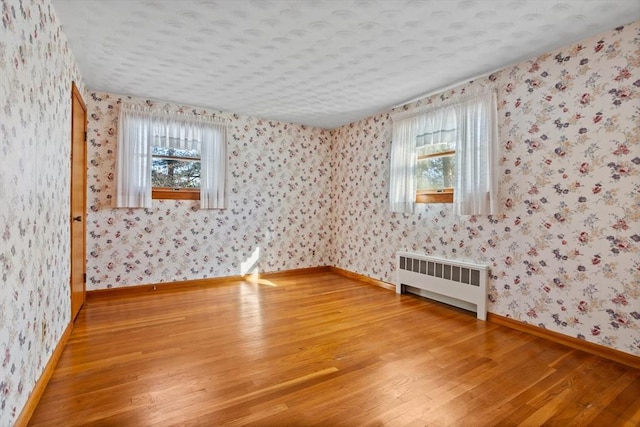 unfurnished room with radiator, hardwood / wood-style floors, and a wealth of natural light