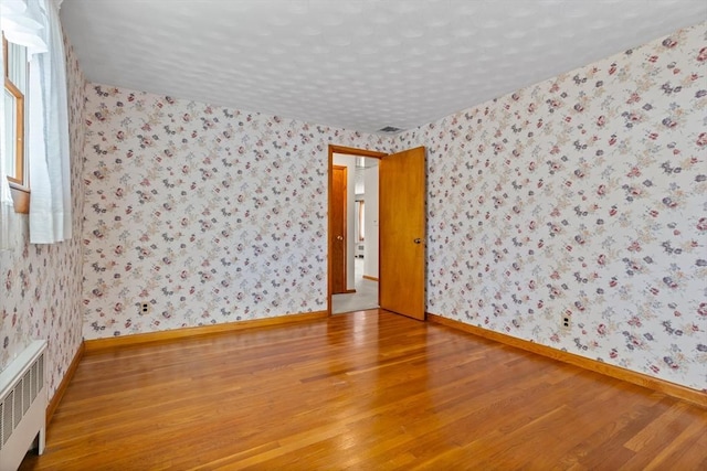 spare room featuring radiator, hardwood / wood-style floors, and a textured ceiling