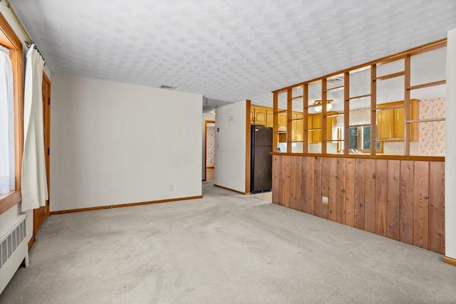 spare room with radiator, light colored carpet, and wood walls