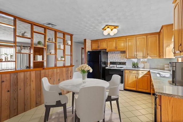 kitchen with light tile patterned flooring, white electric range oven, black fridge, a kitchen breakfast bar, and backsplash