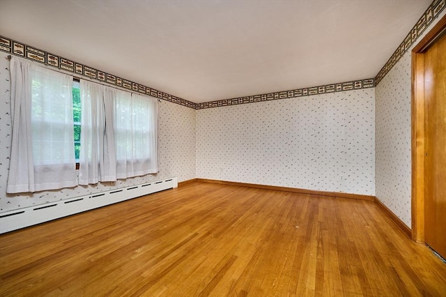 unfurnished room featuring baseboard heating, wallpapered walls, wood finished floors, and baseboards