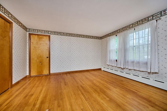 unfurnished room with wallpapered walls, wood finished floors, a baseboard radiator, and baseboards