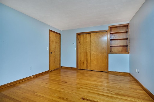 unfurnished bedroom featuring light wood-style flooring, baseboards, and a closet