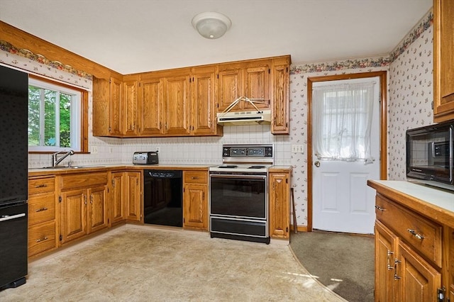 kitchen with black appliances, under cabinet range hood, light countertops, brown cabinetry, and wallpapered walls