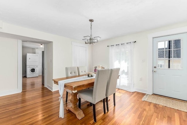 dining room with stacked washing maching and dryer, baseboards, light wood-style flooring, and a notable chandelier