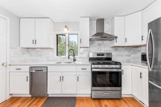 kitchen featuring wall chimney range hood, light countertops, stainless steel appliances, and a sink