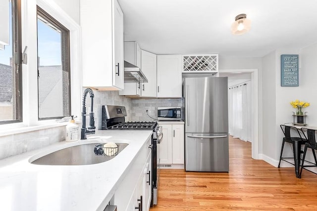 kitchen with ventilation hood, a sink, light countertops, stainless steel appliances, and white cabinetry