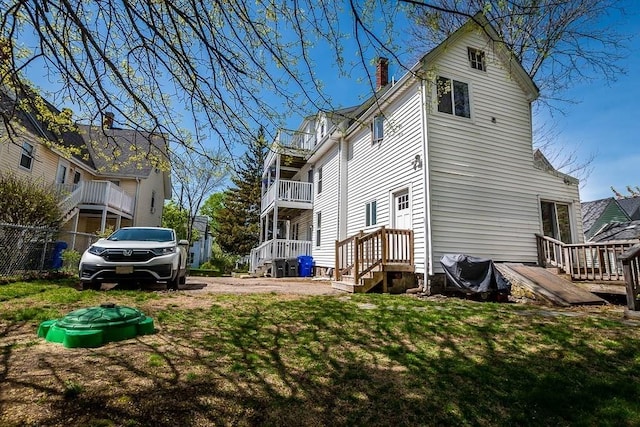 back of house featuring a lawn, a chimney, and a balcony