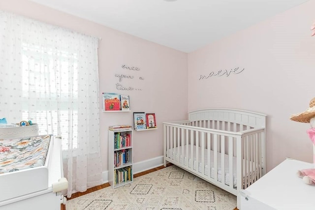 bedroom with baseboards, a crib, and wood finished floors