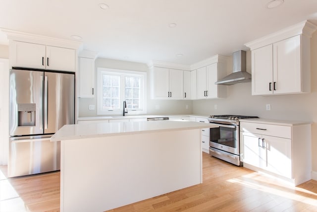 kitchen featuring white cabinetry, a center island, wall chimney exhaust hood, stainless steel appliances, and light hardwood / wood-style floors