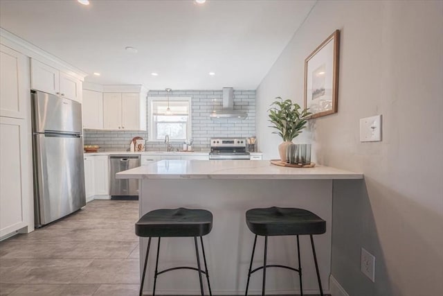 kitchen with a kitchen breakfast bar, sink, wall chimney exhaust hood, appliances with stainless steel finishes, and white cabinetry