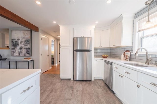 kitchen with appliances with stainless steel finishes, sink, beam ceiling, white cabinets, and hanging light fixtures