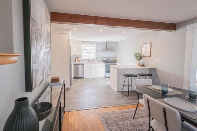 kitchen featuring a kitchen breakfast bar, wall chimney range hood, electric range, dishwasher, and white cabinetry