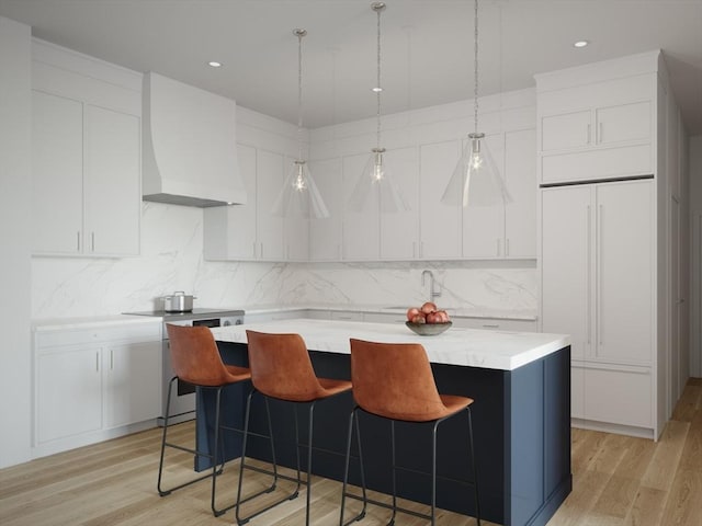 kitchen featuring stove, white cabinets, wall chimney range hood, light hardwood / wood-style flooring, and a kitchen island