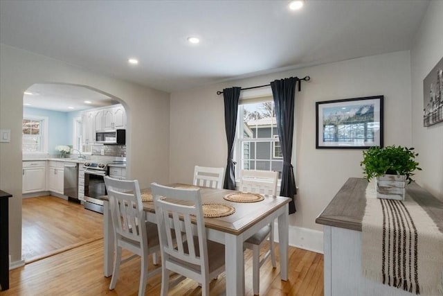 dining space featuring recessed lighting, a healthy amount of sunlight, arched walkways, and light wood finished floors