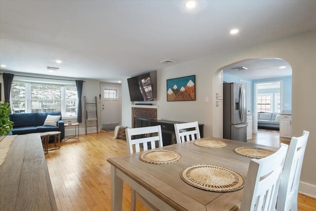 dining area featuring light wood finished floors, visible vents, recessed lighting, a fireplace, and arched walkways