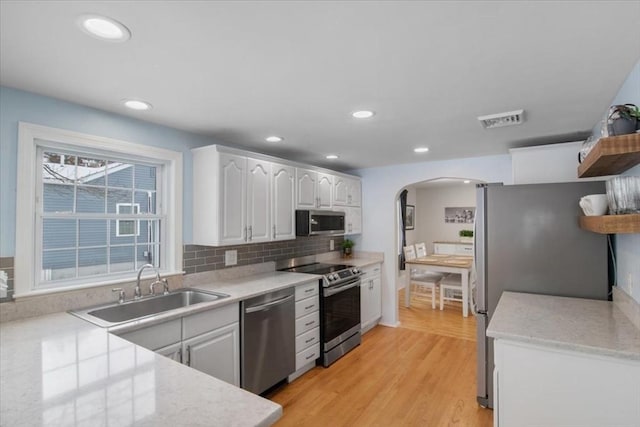 kitchen featuring visible vents, a sink, open shelves, arched walkways, and appliances with stainless steel finishes